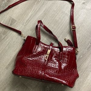 Crocodile maroon colored handbag with crossbody strap.